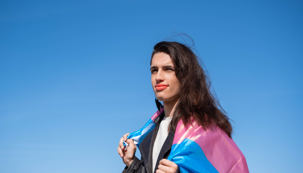 Photo of a person with a transgender flag draped over their shoulders